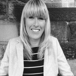 Black and white image of Stephanie smiling in front of a stone wall