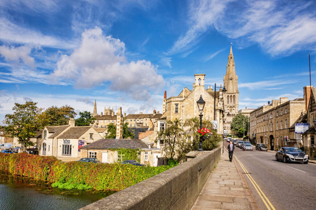 A view from a stone bridge looking towards Stamford with stone buildings and the spires of two churches in view