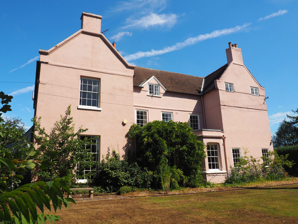 A view of a pale pink rendered listed Rectory located in Epperstone