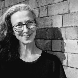 Black and white photograph of Anne smiling next to a brick wall