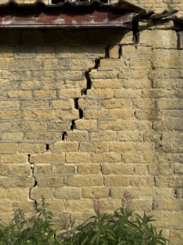 A heavily cracked external stone wall to an outbuilding